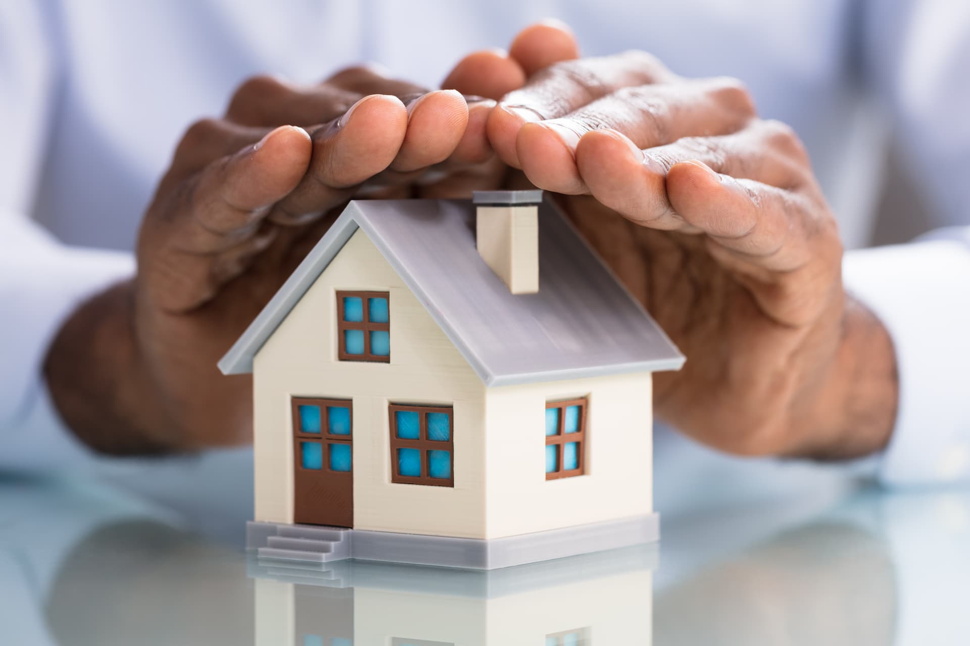 Mains protégeant une maquette de maison